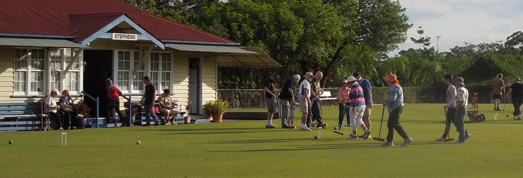 The cream weatherboard Stephens clubhouse with its sign, members playing on the lawn beside it