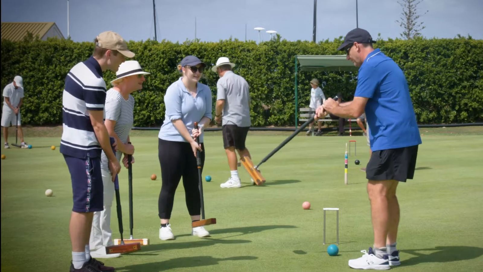 A coach showing new players how to hold a mallet on a croquet lawn