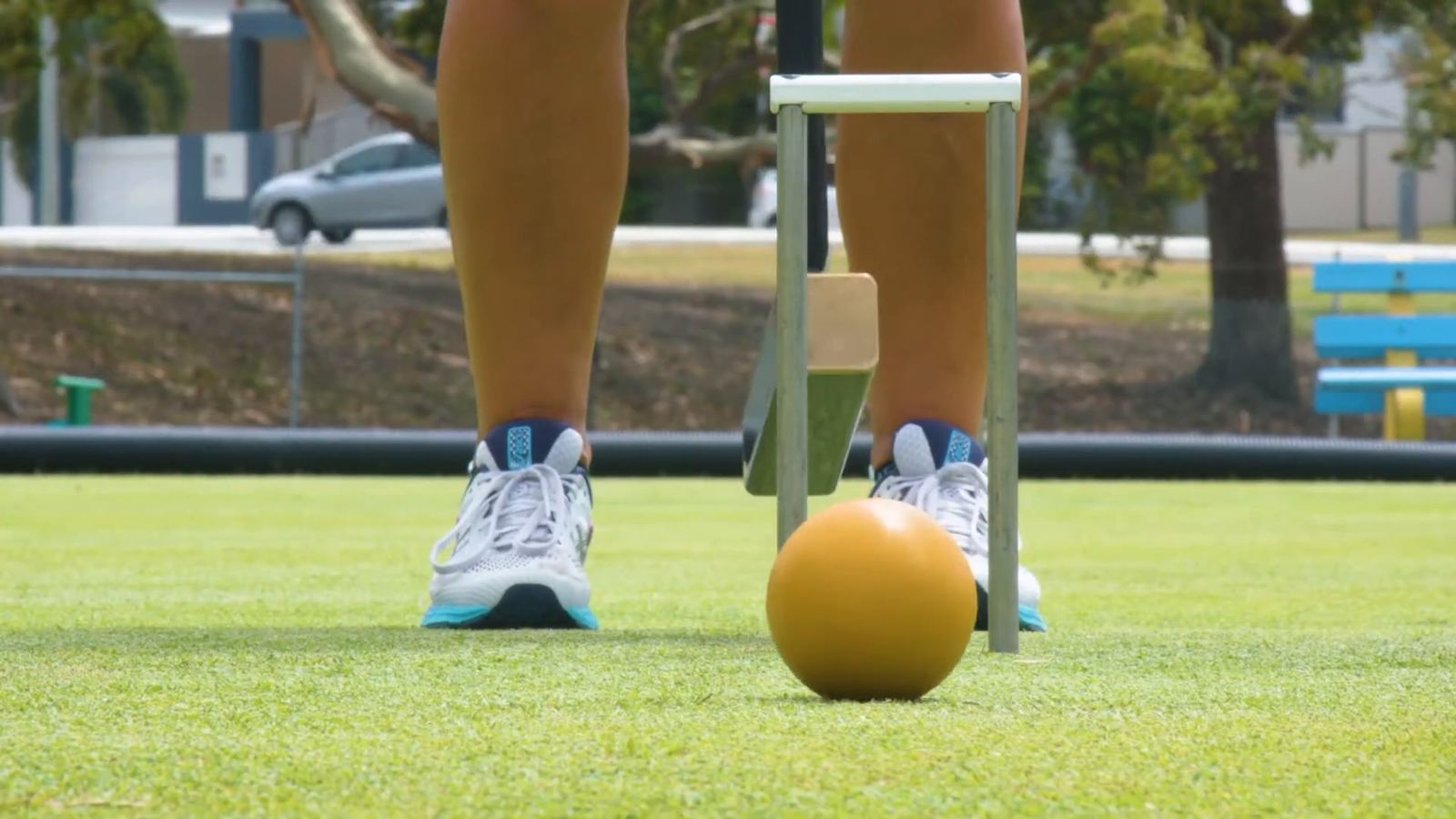 A yellow ball rolling away from a player's feet, a hoop behind